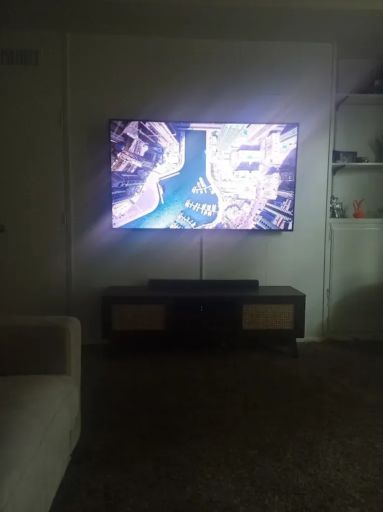 A television mounted on a wall above a media console, displaying a digital map in a dimly lit room.