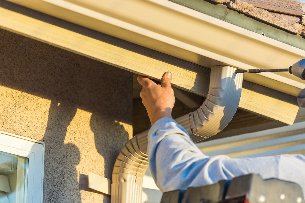 a man is fixing a gutter on a house with a drill .