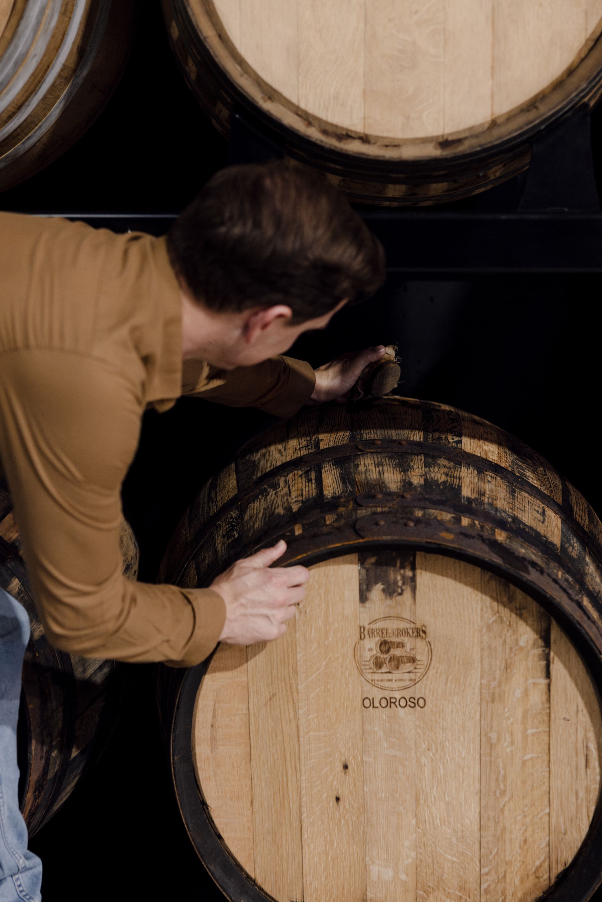 Distiller inspecting whisky barrel during maturation process in Australian distillery.