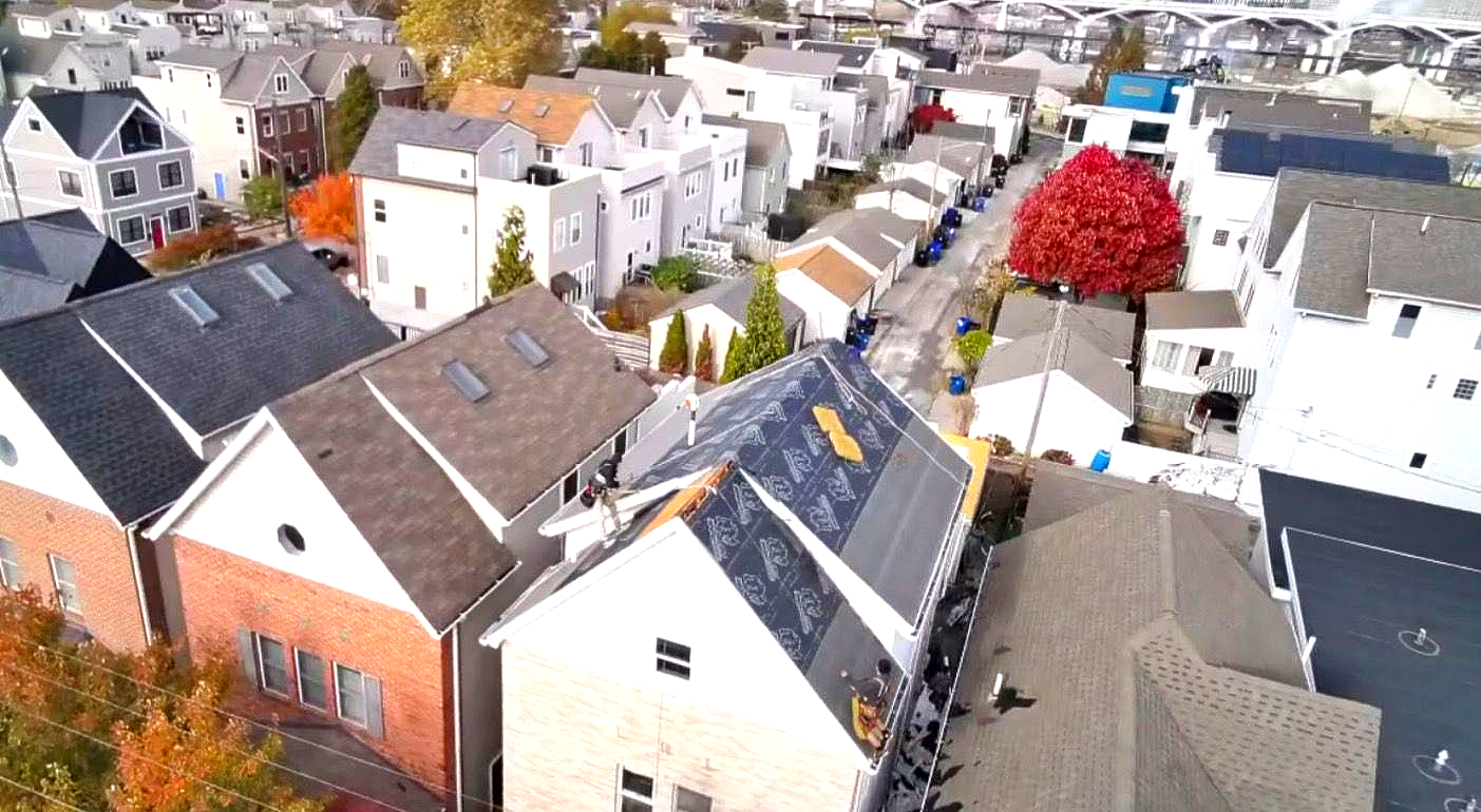 Aerial view of a dense neighborhood with rows of houses and a bright red tree in autumn.