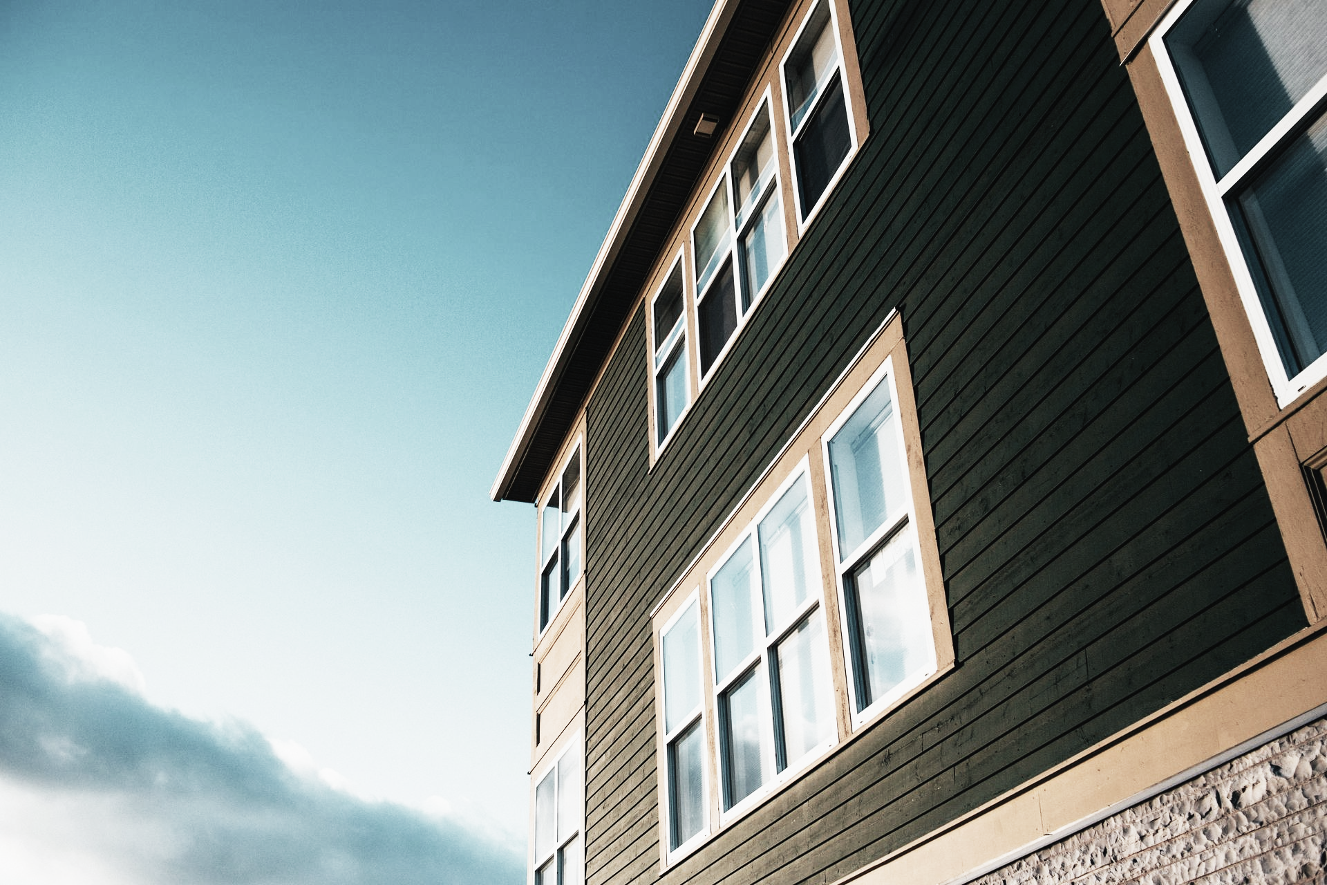 Modern house exterior with dark siding, tan trim, and large windows against a blue sky