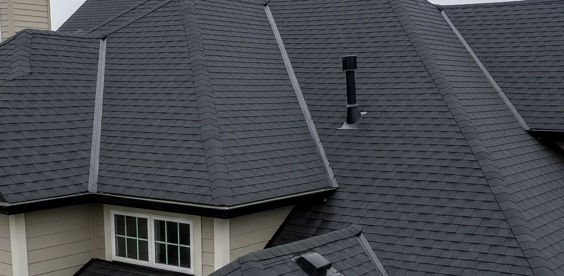 Dark gray shingled roof with white-trimmed dormers and a chimney vent