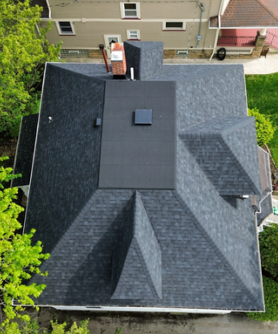 Aerial view of a dark shingle roof with multiple gables and a central flat-roofed section.