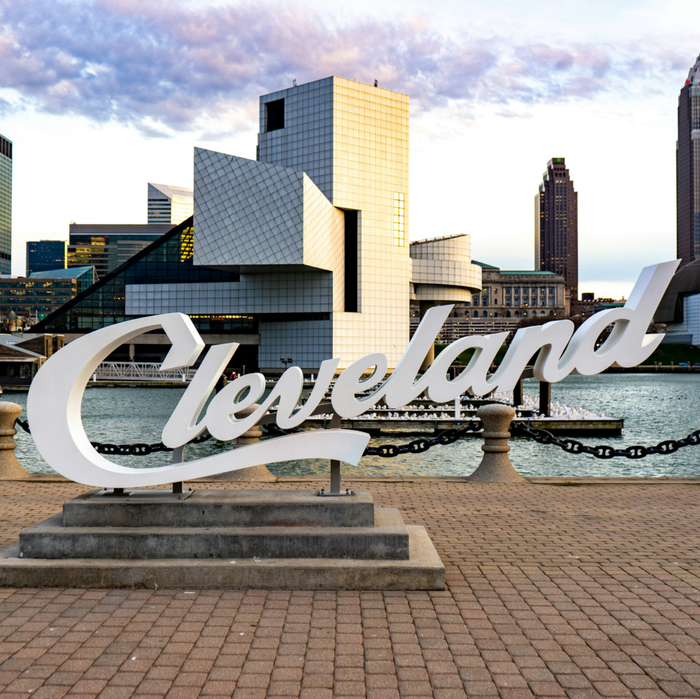 Cleveland sign on waterfront with city skyline and buildings in the background, under a cloudy sky