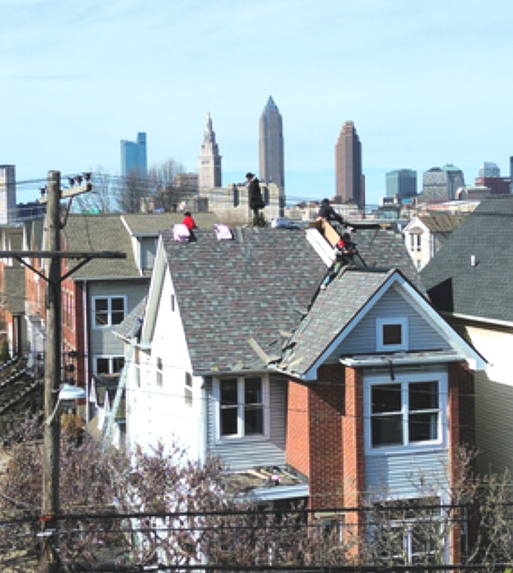 Rooftops of houses in front of a city skyline on a clear day.