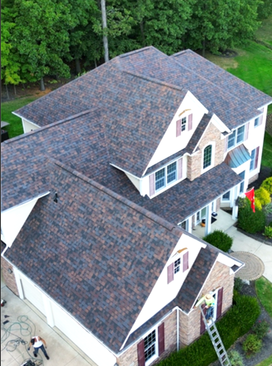 Aerial view of a two-story house with a dark shingled roof, white siding, blue shutters, and a ladder by the entrance
