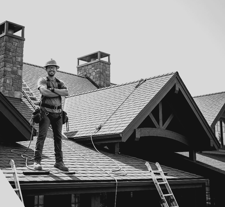 Worker standing on a roof beside a ladder, inspecting shingles on a house with chimneys.
