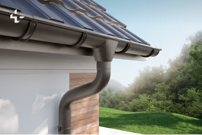 Rain gutter and downspout on a house roof, with green yard and trees in the background