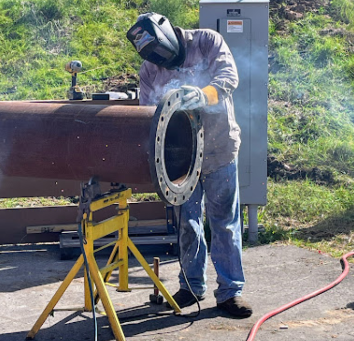 A man wearing a welding mask is welding a pipe