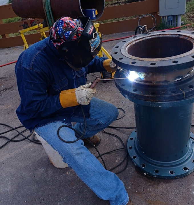 A man wearing a welding helmet is welding a pipe