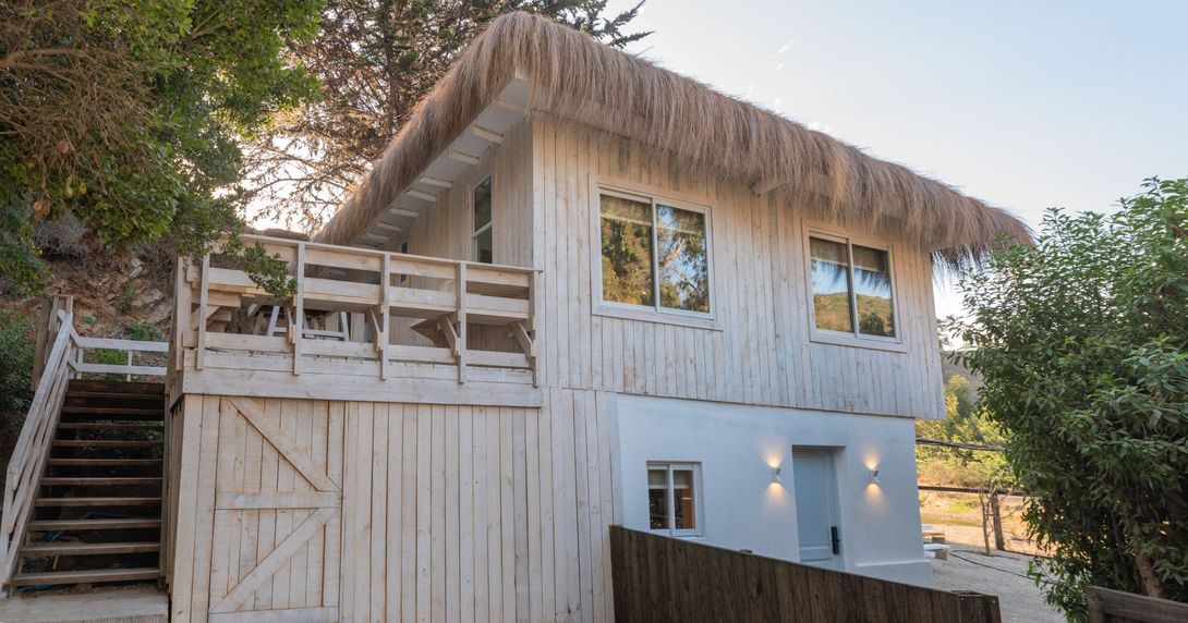 una pequeña casa de madera con techo de paja y escaleras que conducen a ella.