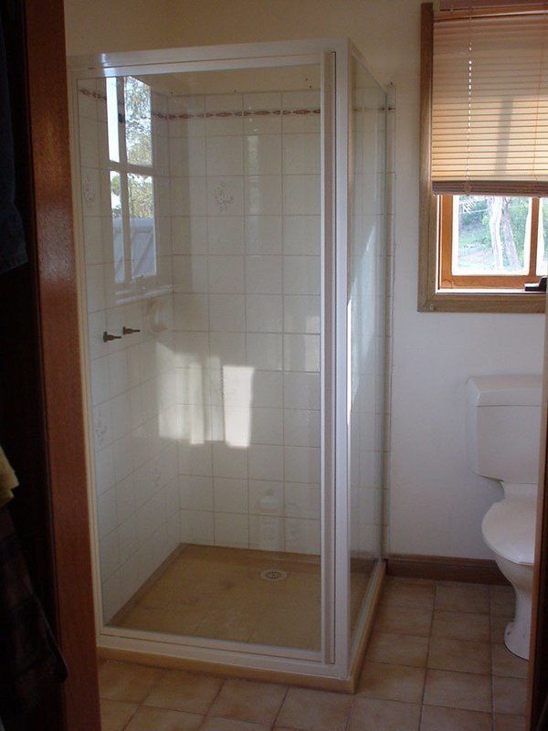 Shower stall in a bathroom with beige tiles and a window with blinds.