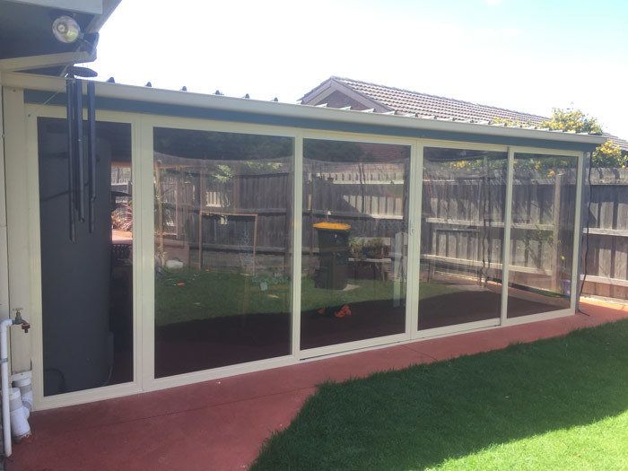 Outdoor enclosure with clear glass panels, attached to a house with a red patio and grass.