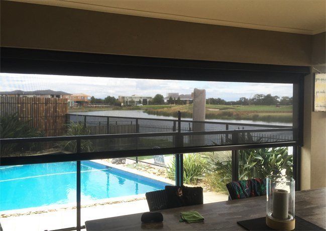 View through open blinds of a pool, lake, and houses.