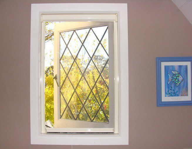 Open window with diamond-patterned glass, white frame, tan wall, and a blue framed picture.