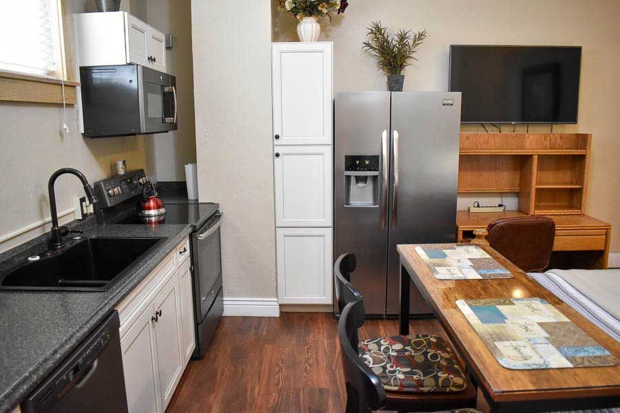 Modern kitchen and dining area with stainless steel fridge, black countertops, and a wooden table set for a meal