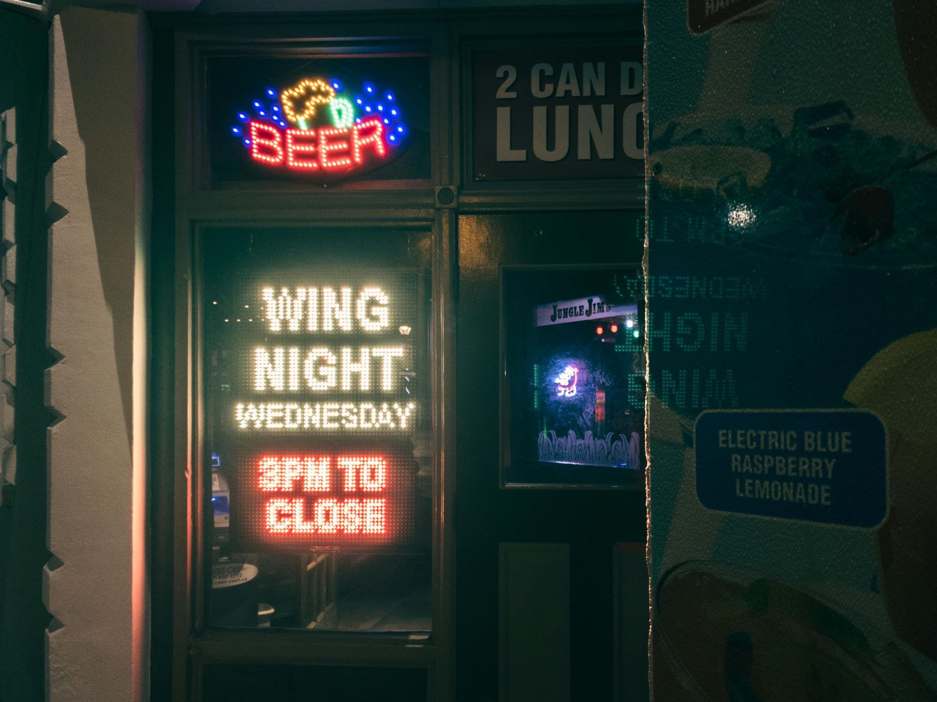 Neon bar signs advertising beer and Wing Night Wednesday, with “5 PM to close” glowing in red.
