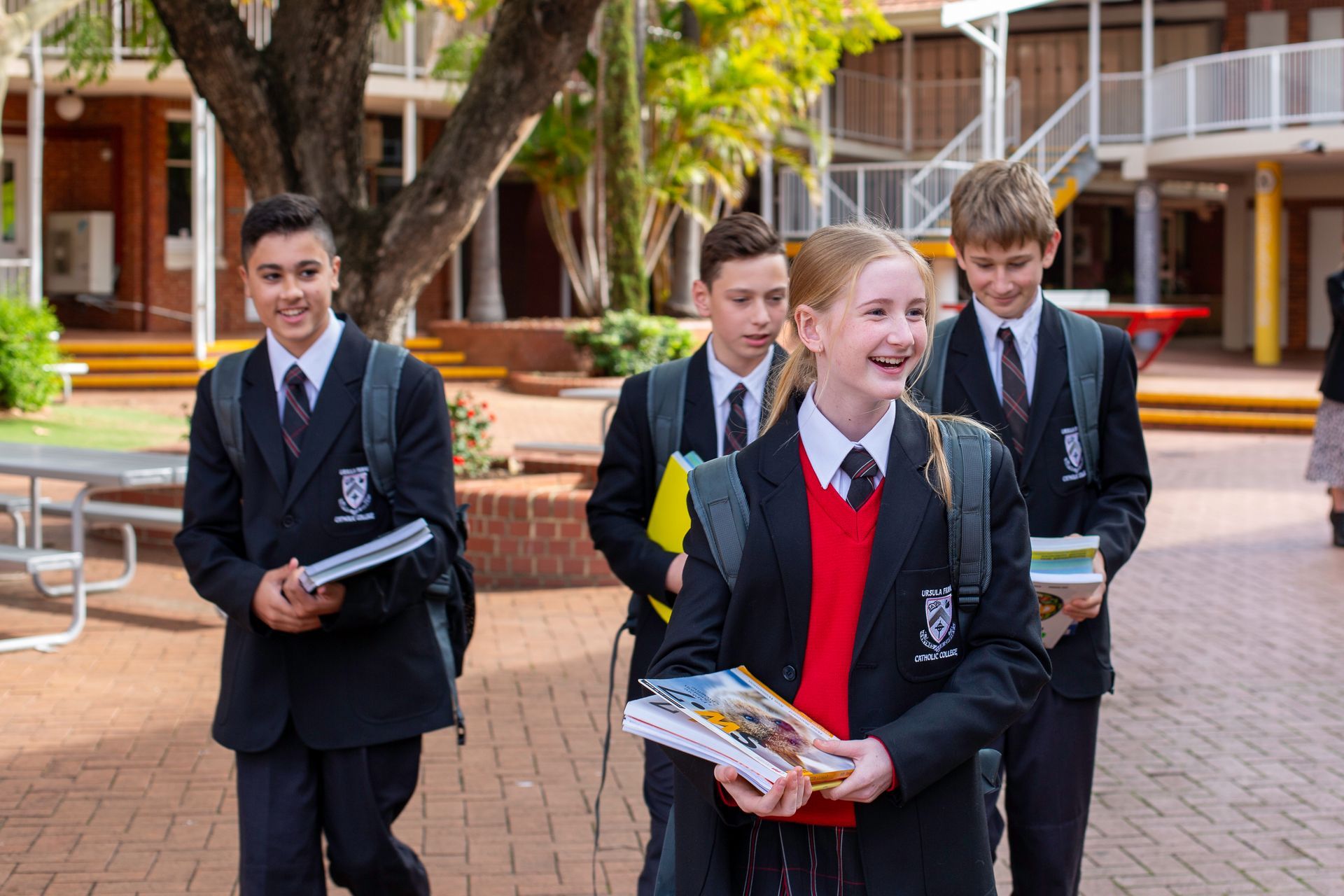 School students in uniform walking and smiling on campus, holding books.