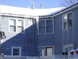 a blue house with snow on the roof and icicles on the windows