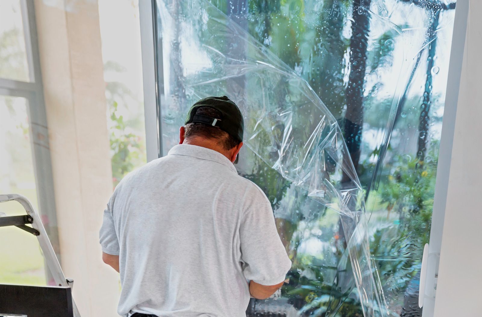 A man is covering a window with plastic.
