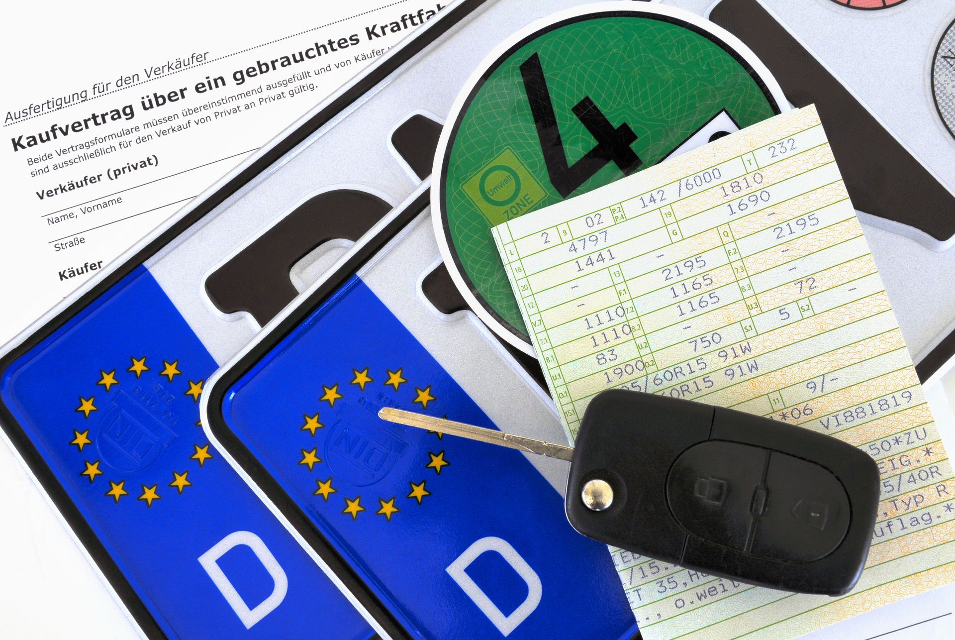 Zwei blaue Nummernschilder, ein grüner Aufkleber, ein Autoschlüssel und eine Quittung, wahrscheinlich für den Verkauf eines Gebrauchtwagens.