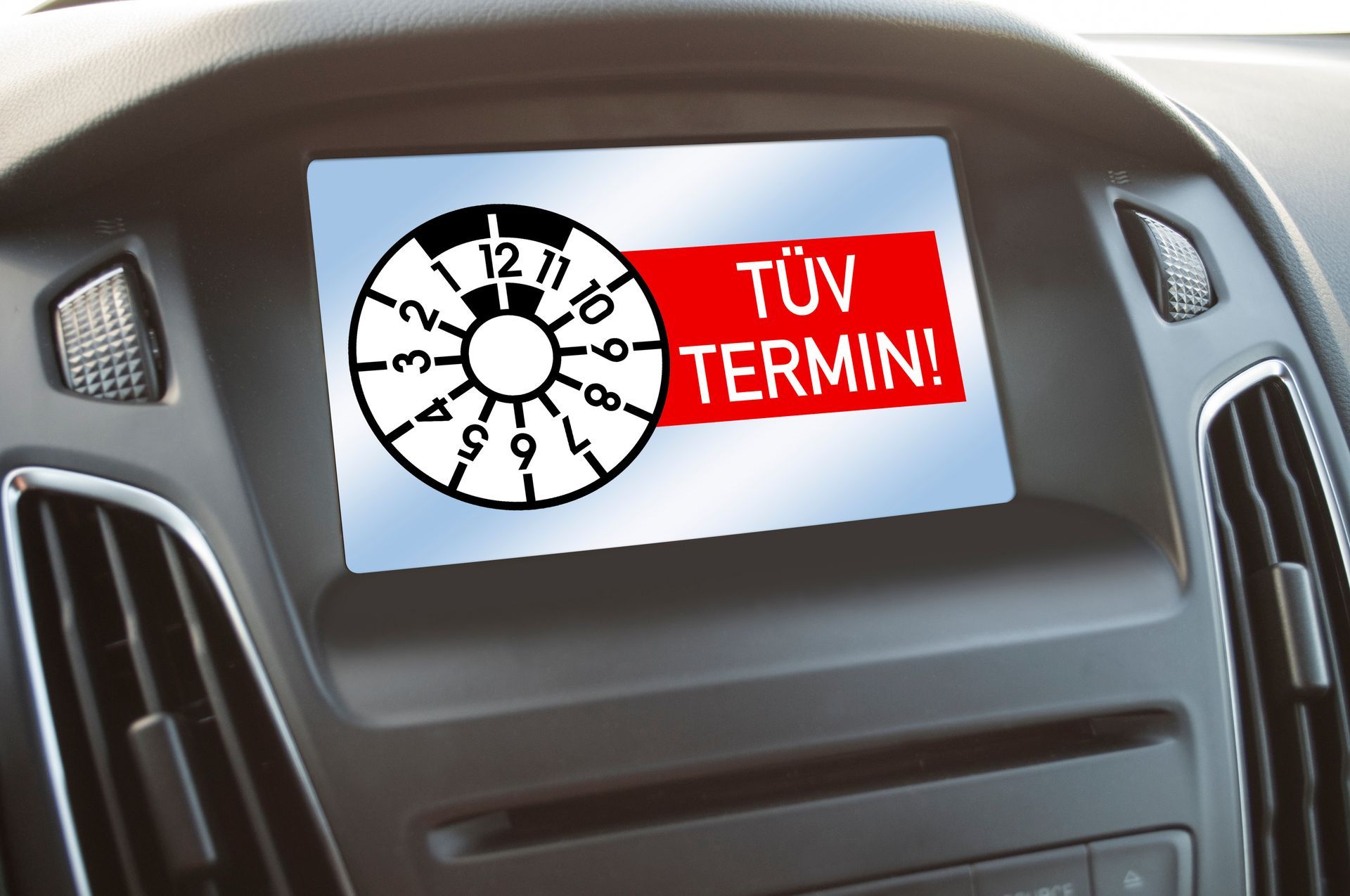 Auf dem Armaturenbrettbildschirm werden ein runder Prüfaufkleber und eine rote „TÜV TERMIN!“-Warnung angezeigt.