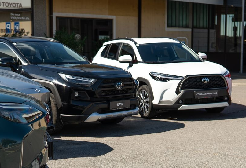 Weißer Toyota RAV4, geparkt vor einem Gebäude mit reflektierendem Glas.