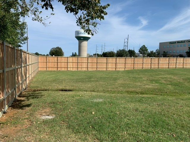 A wooden fence surrounds a grassy field with a water tower in the background.