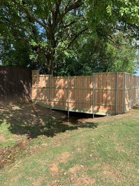 A wooden fence is surrounded by trees in a grassy area.