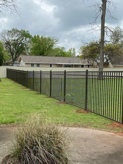 A black fence surrounds a lush green field in front of a house.
