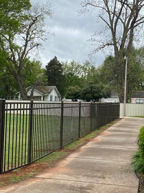 A fence along a sidewalk with a house in the background.