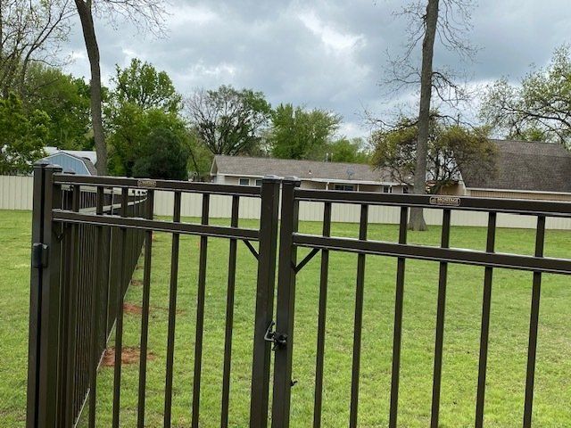 A metal fence surrounds a lush green field with a house in the background.
