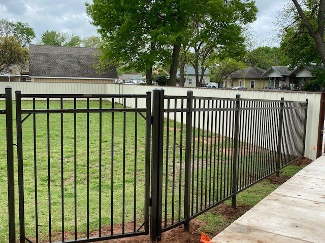 A black metal fence with a gate is surrounding a lush green field.