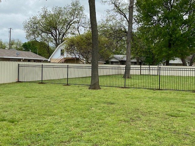 A fence surrounds a lush green yard with trees and houses in the background.