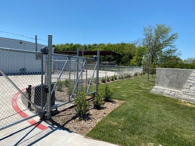 A chain link fence with a sliding gate in front of a building.