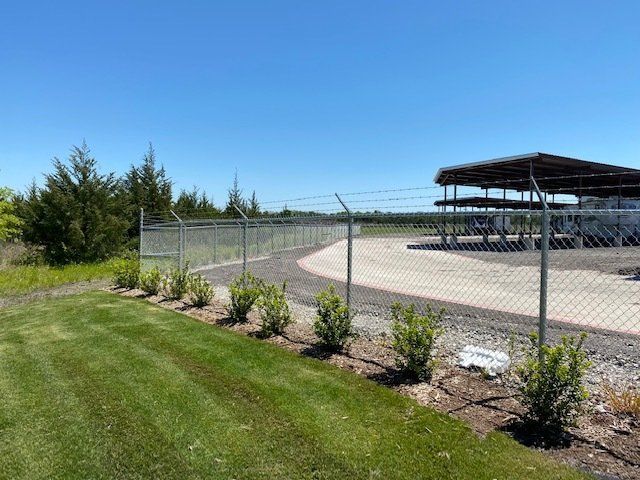 A chain link fence surrounds a parking lot with a building in the background.