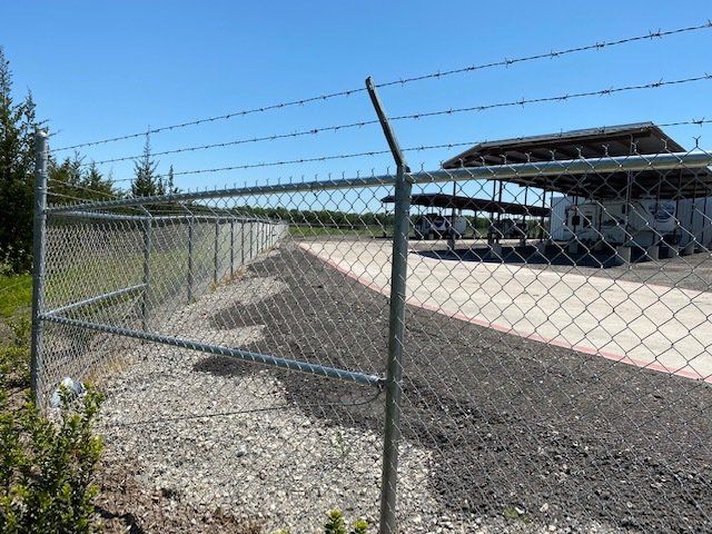 A chain link fence with barbed wire surrounding a parking lot