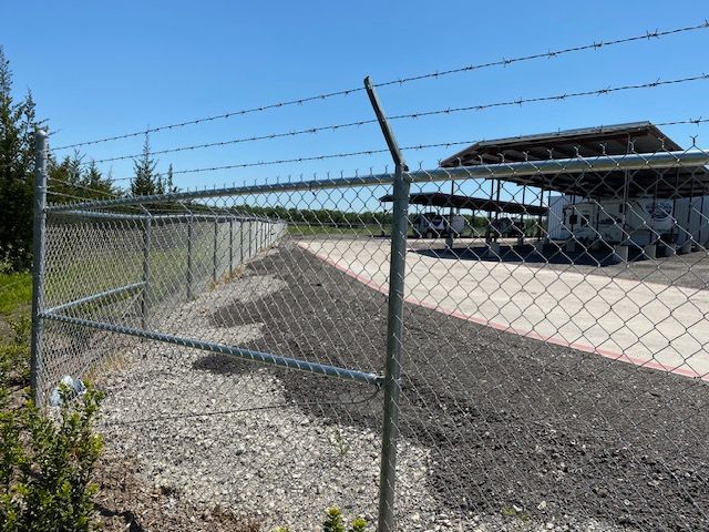 A chain link fence with barbed wire surrounding a parking lot