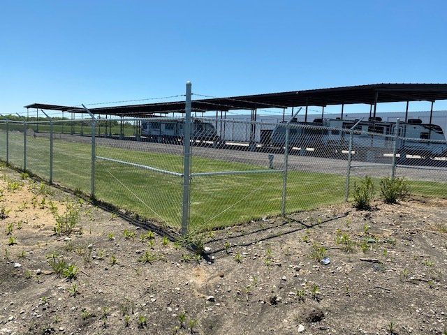 A train is parked under a canopy in a parking lot behind a fence.