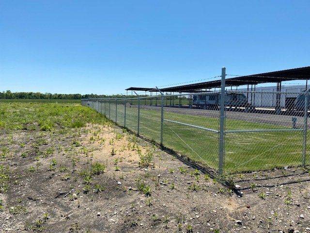 A chain link fence surrounds a field with a building in the background.