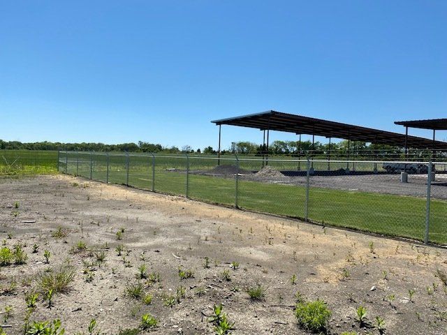 A fence surrounds a field with a covered area in the background