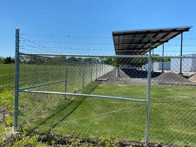 A chain link fence with barbed wire surrounding a field.