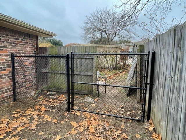 A chain link fence with a gate in the backyard of a house.