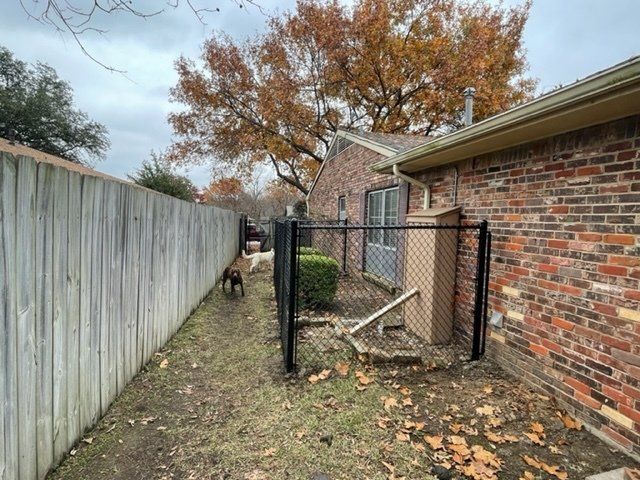 A chain link fence is in the backyard of a brick house.