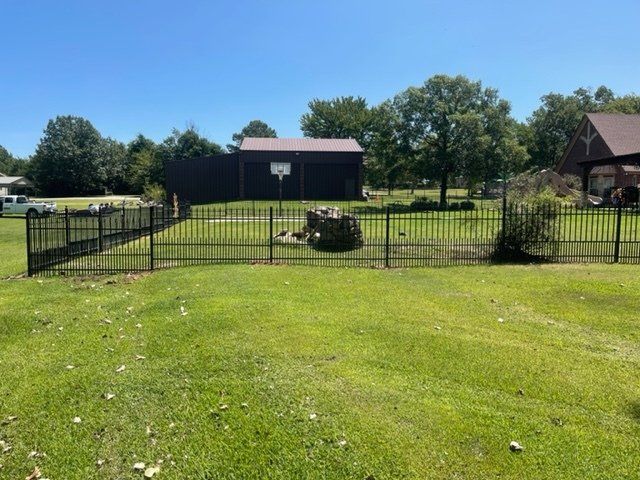 A fence surrounds a lush green field with a basketball hoop in the background.