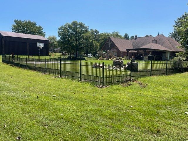 A fence surrounds a lush green field with a house in the background