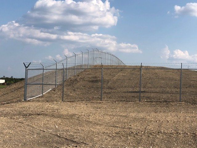 A fence surrounds a dirt hill with a blue sky in the background.