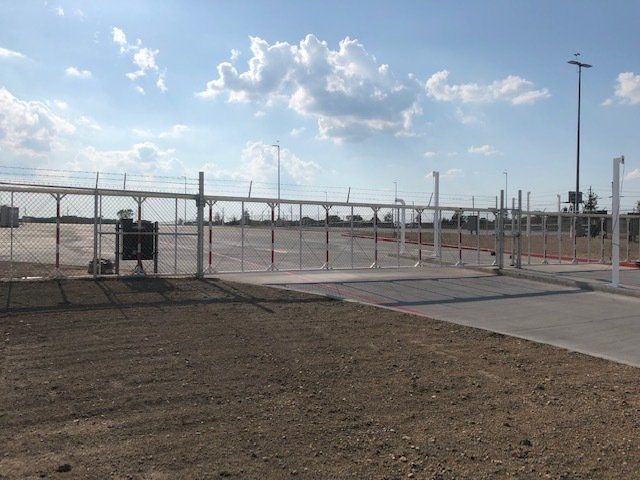 A fence surrounds a dirt field with a blue sky in the background.