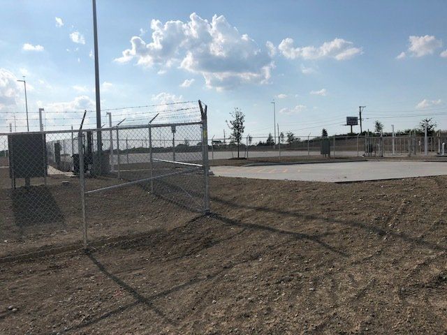 A fence surrounds a dirt field with a basketball court in the background.