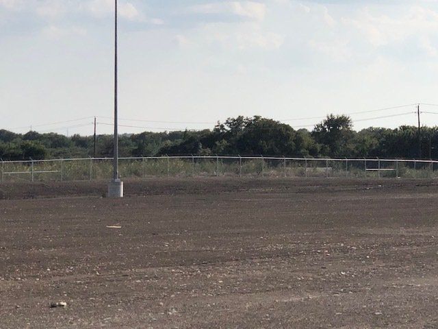 An empty field with a fence and trees in the background